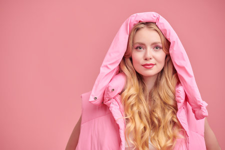 Fashionable pink color. Beautiful blonde girl fashion model posing in trendy pink clothes on a pink studio background. Femininity style. Elegant makeup and hairstyle.の写真素材