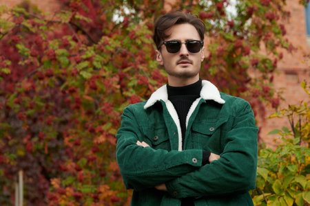 A handsome serious young man in jeans and a corduroy jacket stands in an autumn park. Autumn fashion.の写真素材