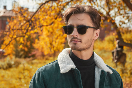 Life moments. Autumn portrait of a handsome young brunet man posing in fashionable denim clothes in an autumn park. Denim style.の写真素材