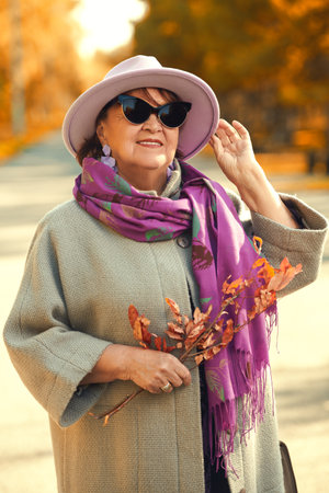 A beautiful and happy elderly woman is walking in an autumn park. Happy retirement age.の写真素材