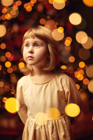 Magic for Christmas and New Year. An angelic little girl surrounded by golden lights looks up at the light waiting for a miracle.の写真素材