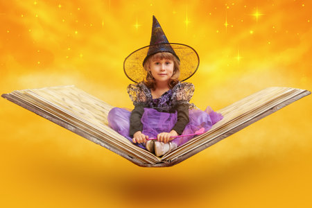 A little witch girl flies through the sky on a big book of spells. Fairytale background with starry sky and golden clouds. Halloween. Fairy tales for children.の写真素材