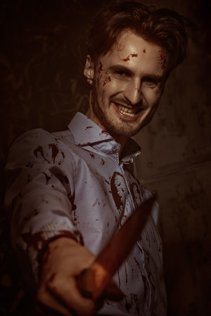 Portrait of a crazy killer maniac standing in the dark with a bloody knife. Thriller, horror.の写真素材