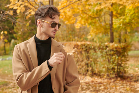 Life moments. A handsome man with dark wavy hair, dressed in a classic drape coat, stands in an autumn park. Autumn fashion. Copy space.の写真素材