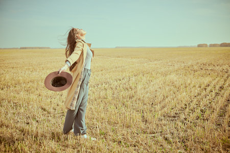 Happy moments. A happy young woman stands in an autumn field, spreading her arms to the sides and turning her face to the wind. Life concept. Feeling of freedom. Copy space.の写真素材
