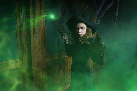 A fairy-tale witch girl casts a spell with a magic wand, standing in an old house. Halloween.の写真素材