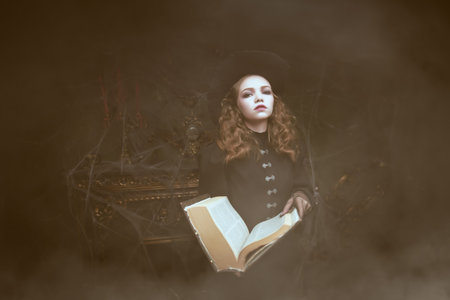 Tales of magic. A young witch stands with an open book of spells in an old castle shrouded in...