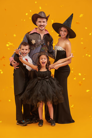 Happy Halloween! A cheerful family of parents and children dressed in carnival costumes is having fun celebrating Halloween. Magic background with golden clouds and stars.の写真素材