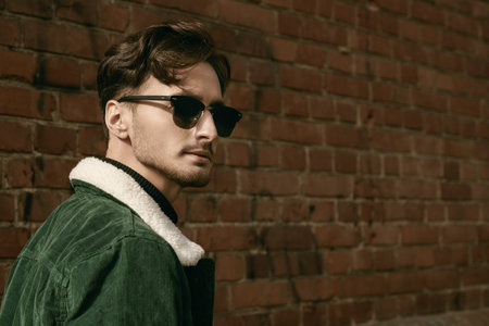 Autumn fashion style for men. Portrait of a handsome brunette man, a fashion model, posing on the street near a brick wall in black jeans and a green corduroy jacket.の写真素材
