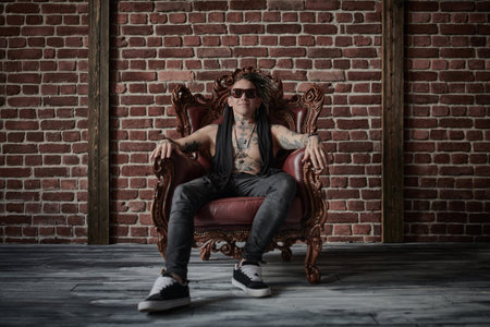 Rock style. A cool rock musician with tattoos and a mohawk of dreadlocks on his head poses in a...