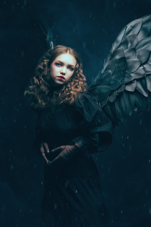 Fantasy. Halloween. A beautiful black angel girl in a black dress stands alone in the dark, expressing grief and sadness. Black background.の写真素材