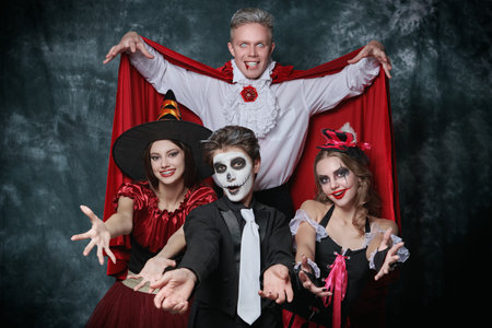 Merry Halloween party. Portrait of a teenage friends in carnival costumes having fun celebrating Halloween. Skeleton, witch, clown and vampire. Studio portrait.の写真素材
