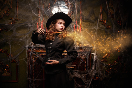 A fairytale witch girl casts a spell with a magic wand, standing in an old house. Halloween.の写真素材