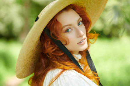 A beautiful romantic girl with charming wavy red hair, dressed in a long white shirt and a...