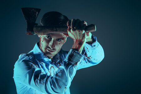 An angry man killer maniac, covered in blood, holds an ax over his head. Horror, thriller. Dark studio background with copy space.の写真素材