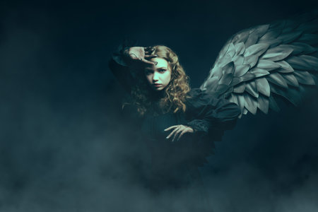 Dramatic black angel girl in a black dress spreads her wings, looking determinedly at the camera,...