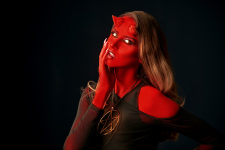 Scary fantasy heroes. A seductive she-devil with bloody horns stands  on a black background. Halloween. Place for text.の写真素材