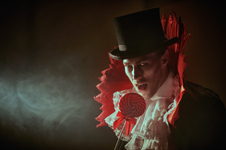 Novels and movies about vampires. A handsome, elegant male vampire in a 19th century style suit looks enticingly into the camera and holds out a lollipop in his hand. Halloween. Copy space.の写真素材