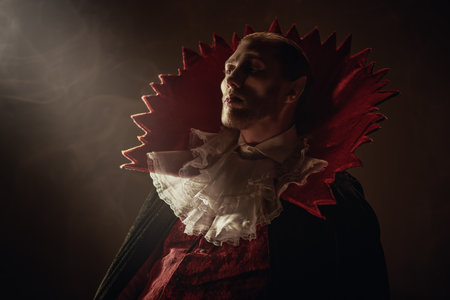 Vampires. Portrait of an imposing male vampire in an elegant vintage suit with a cape, standing in the dark and looking ahead calmly and thoughtfully. A beam of light illuminates his face. Halloween.の写真素材