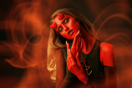 Portrait of a seductive she-devil with bloody horns on a dark fire background. Halloween. Scary...