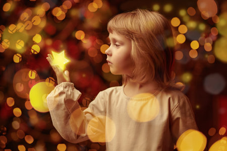 Magic for Christmas and New Year. A little angelic girl stands surrounded by twinkling lights and touches a small golden star. Copy space.の写真素材