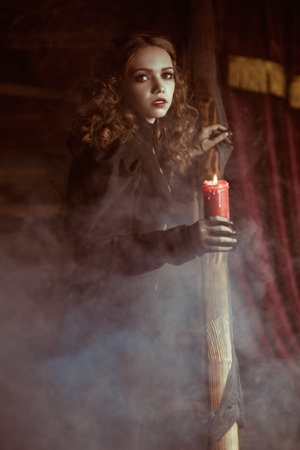 A pale, frightened lady in a black dress climbs a wooden staircase with a candle in her hand in a dark ancient castle. Historical and mystical novel. Victorian style. Halloween.の写真素材