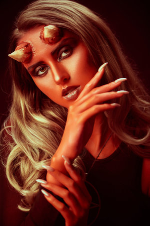 Close-up portrait of a magnificent and terrible devil girl with bloody horns on a black background....