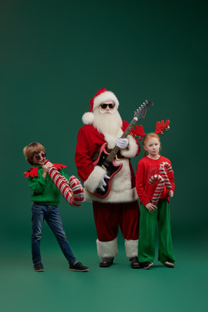 Two joyful kids with Santa Claus ready for a cool Christmas party. Celebration of Christmas and New Year. Music, disco. Green studio background with copy space.の写真素材
