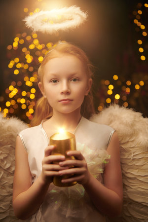 A shot of a little girl wearing a costume of angel holding a candle and dreaming in beautiful Christmas setting. Merry Christmas and Happy New Year!の写真素材