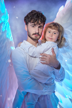 A male angel holds a happy little girl in his arms and protects her. Heavenly mixed light. Christmas and New Year.の写真素材