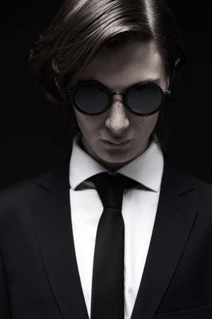 Men's fashion and style. Portrait of a well-groomed young man with stylish hair styling, posing in an elegant black classic suit,  white shirt and elegant sunglasses. Black background.の写真素材