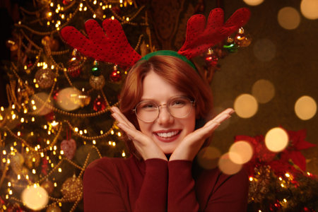 A joyful red-haired wearing deer horns stands in a beautiful Christmas setting and smiles dreamily. Christmas and New Year celebration.の写真素材