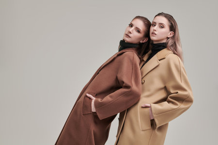 Demi-season women's fashion. Portrait of two fashion models of girls posing in stylish felt coats. Studio white background.の写真素材