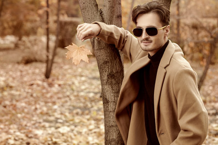 Life moments, emotions. A handsome man with dark wavy hair, dressed in a classic drape coat, stands in an autumn park. Autumn fashion. Copy space.の写真素材