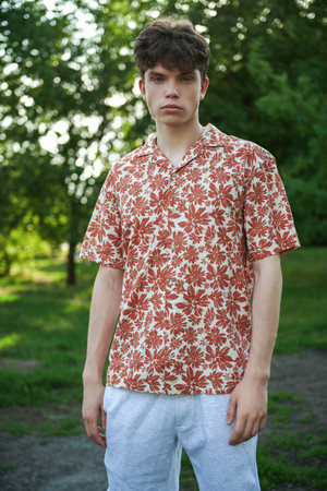 Portrait of a handsome young man in a summer shirt and shorts against the background of trees in a summer park. People, life moments, emotions. Summer time.の写真素材