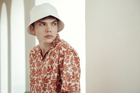 Summer fashion. Portrait of a modern young man in a summer shirt and white panama against a white wall. Street shot. People, life moments, emotions.の写真素材