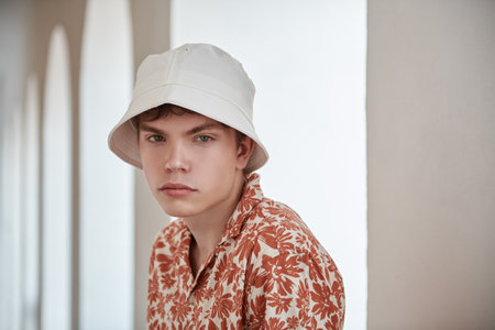 People, life moments, emotions. Summer fashion. Portrait of a modern young man in a summer shirt and white panama against a white wall. Street shot.の写真素材