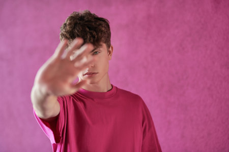 Portrait of a modern young man fashion model in a crimson t-shirt covering his face on a purple background with copy-space. Youth Fashion. Men's hairstyles.の写真素材