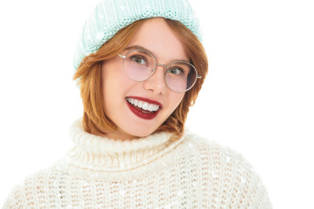 Happy people. Portrait of a cute red-haired girl in warm knitted clothes smiles joyfully at the camera. Portrait on a white studio background with copy space.の写真素材