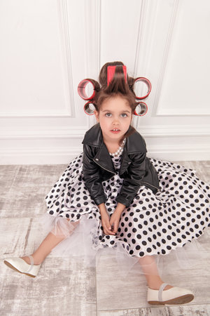 A little fashionista girl in a smart dress with polka dots, in a leather jacket and with curlers on her head is going to a party. Children's Fashion. Pin-up style.の写真素材