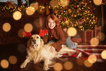 Christmas and New Year. A happy girl celebrates Christmas sitting under a Christmas tree with her dog in the cozy fairy-tale setting of her home.の写真素材