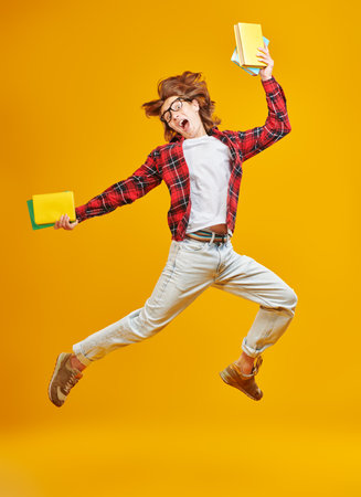 A modern teenager boy in casual clothes jumps with books. Yellow studio background. People and emotions. Education.の写真素材