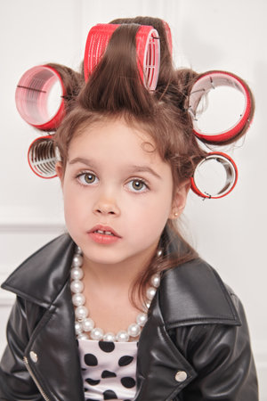 Pin-up fashion style. A little fashionista girl in a smart dress with polka dots, in a leather jacket and with curlers on her head is going to a party. Children's Fashion.の写真素材