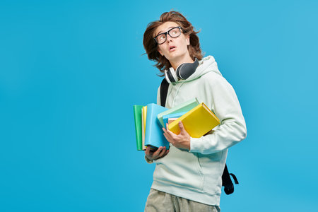 Modern education. A modern high school student holds textbooks and is very surprised. Blue studio background with copy space.の写真素材