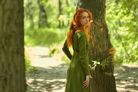 Celtic culture. Fantasy world. Portrait of a beautiful red-haired girl of the Middle Ages walking in the dense forest.の写真素材