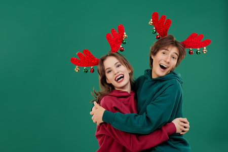 Cheerful young guy and girl congratulate and hug each other on New Year and Christmas. Green studio background with copy space.の写真素材