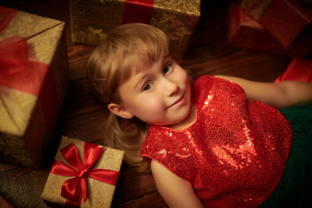 Children's Christmas and New Year. A cute emotional little girl lies under a fir tree surrounded by gifts and screams cheerfully.の写真素材