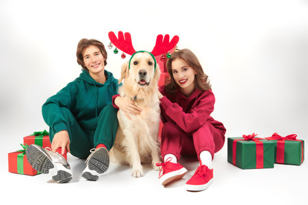 Merry Christmas and New Year. Beautiful smiling teenage friends - a girl and a boy - are posing cheerfully with a cute smiling dog in deer horns. White studio background with copy space.の写真素材