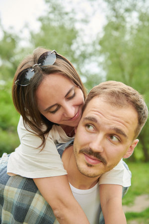 A happy family. A cheerful young man rides his beloved woman on his back. Walk in the summer park.の写真素材