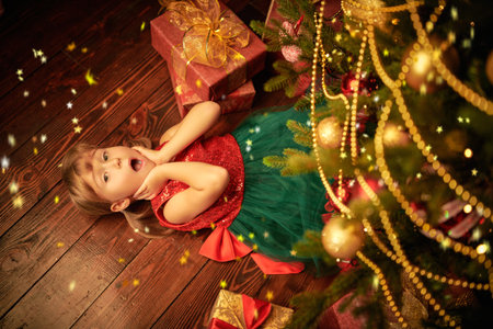 A cute emotional little girl lies under a fir tree surrounded by gifts and screams cheerfully. Children's Christmas and New Year.の写真素材